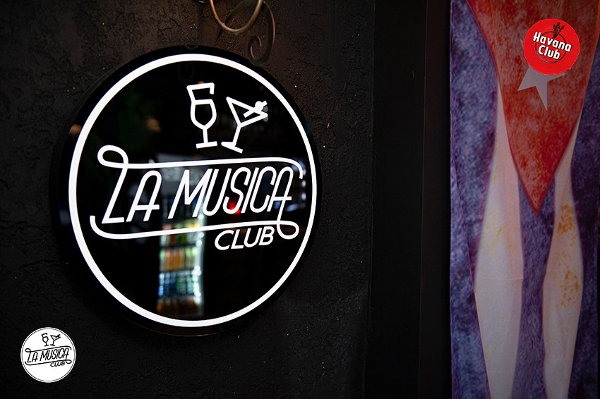 Podświetlany szyld 'La Musica Club' z grafiką kieliszka i drinka, obok plakat z motywami kubańskimi i logo Havana Club.